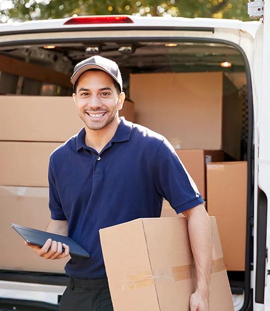Smiling delivery person holding a package and a tablet, standing in front of an open delivery van filled with boxes.